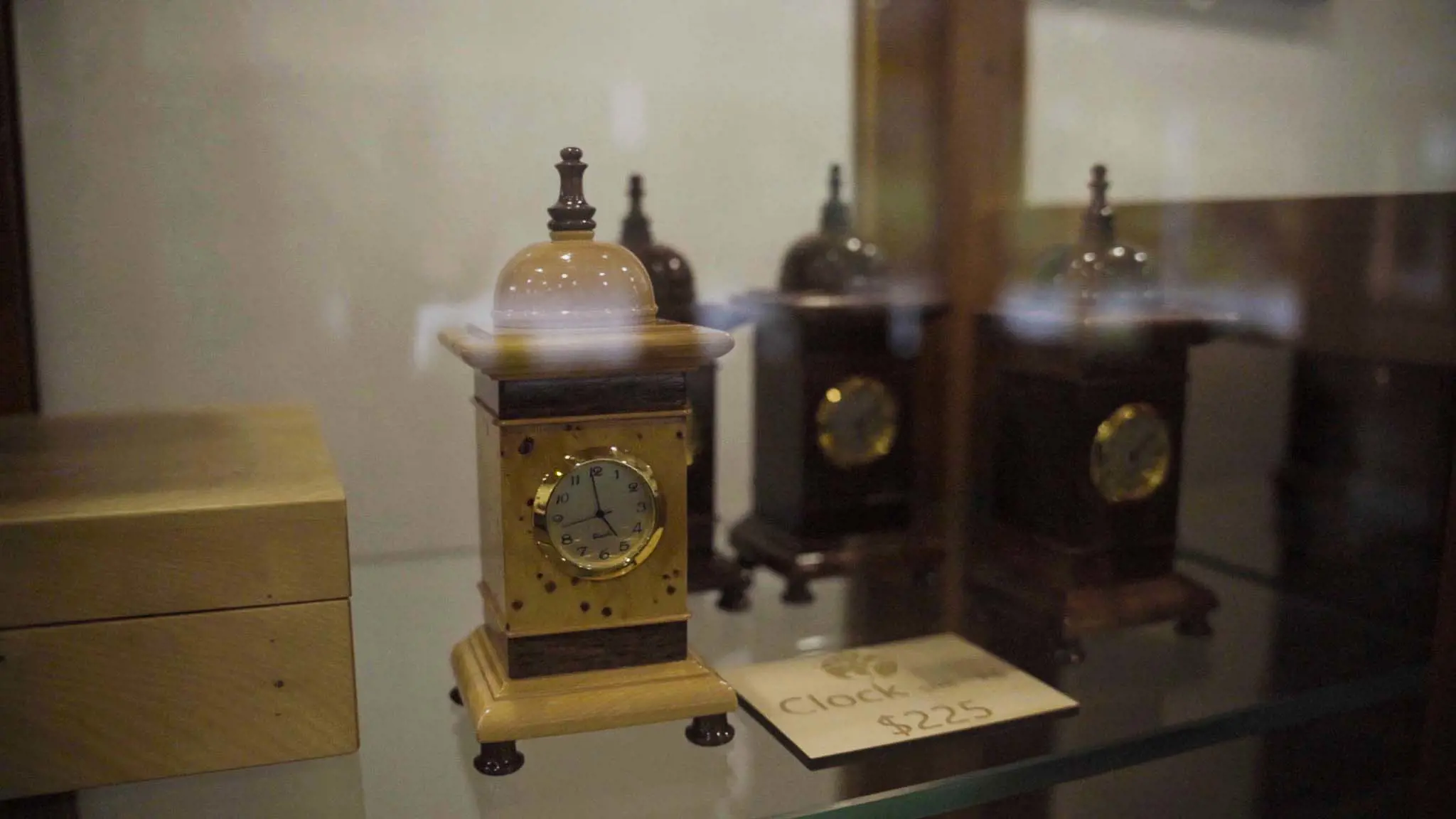 A traditionally styled clock made of light-coloured wood is displayed inside a glass case. 